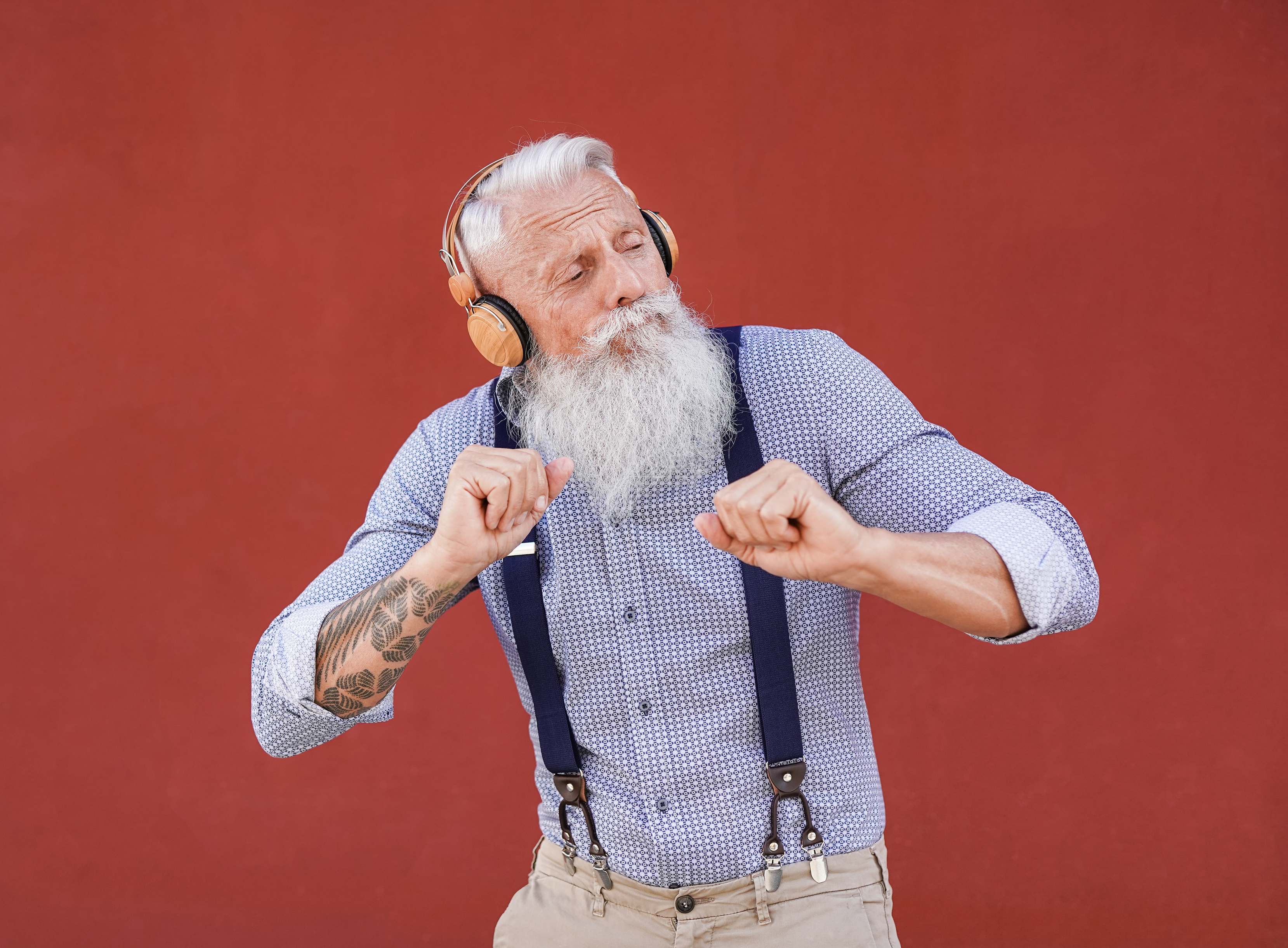 homme-senior-hipster-dansant-plein-air-tout-ecoutant-musique-ecouteurs-sans-fil-fond-rouge.jpg
